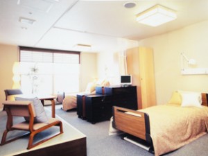 木製ベッドと椅子が配置された個室。窓からの採光で明るい居住空間。